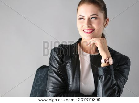 portrait of beautiful young brunette woman in stylish black jacket on gray.