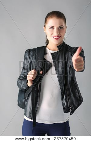 portrait of beautiful young brunette woman in stylish black jacket on gray.