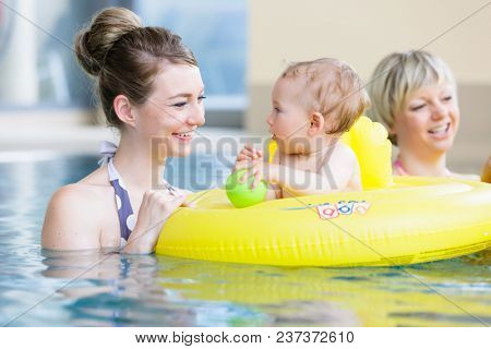 Mums and their children having fun together playing with toys at baby swimming lesson