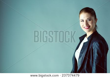portrait of beautiful young brunette woman in stylish black jacket on gray.