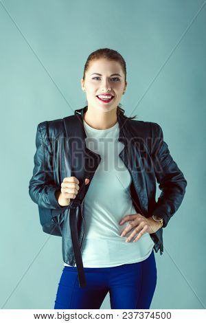 portrait of beautiful young brunette woman in stylish black jacket on gray.
