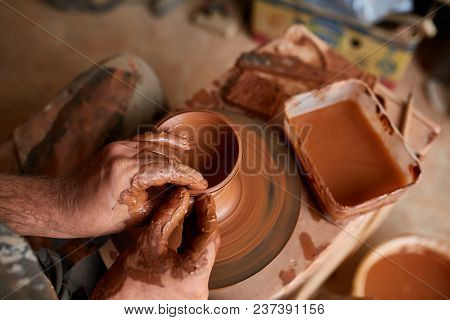 Close-up Hands Of A Male Potter In Plaid Shirt And Dirty Apron Who Molds A Vase From Clay, Selective