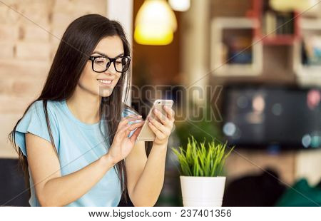 Young Freelancer Girl Wears Blue Shirt And Eyeglasses Using Smartphone For Text Messages In Modern S
