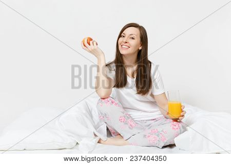 Young Brunette Woman Sits On Bed With White Sheet, Pillow, Wrapping In Blanket Isolated On White Bac