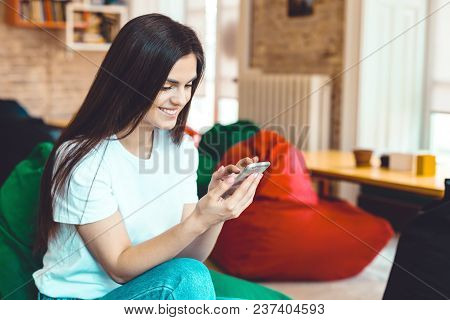 Beautiful Student Girl Using Smartphone For Text Messages In Modern Stylish Coworking Office