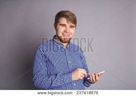 Young Man Texting Message On Smart Phone Isolated On Grey Background. Smiling Guy Holding Smartphone