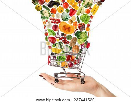 Female Hand Holding Grocery Cart With Vegetables And Fruits Falling In It Isolated On White. Healthy