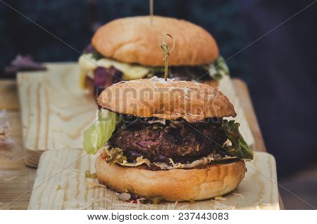 Two Craft Beef Burgers On Wooden Table Isolated On Black Background. The Process Of Making Burger