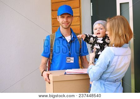 Smiling delivery man in blue uniform delivering parcel box to recipient - courier service concept. Smiling delivery man in blue uniform