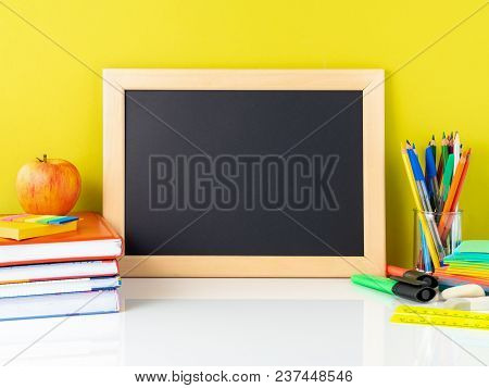 Chalkboard, Apple And School Supplies On White Table By The Yellow Wall. Side View, Empty Space For 