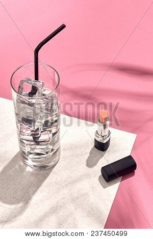 High Angle View Of Lipstick And Drinking Glass With Ice On Table. Pink And White Background With Sha