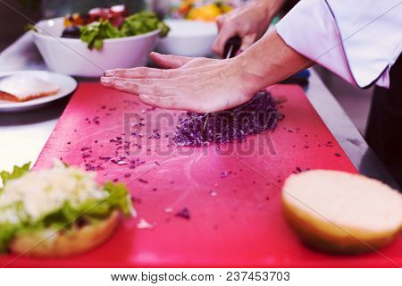 master chef hands cutting salad for a burger in the rastaurant kitchen