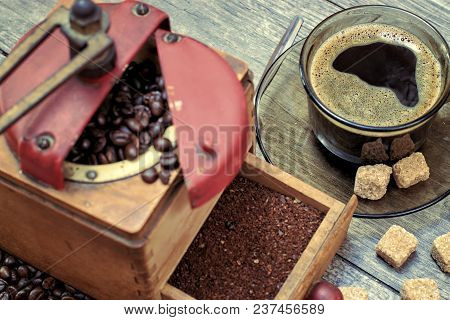 Old Coffee Grinder With A Cup Of Coffee, Coffee Beans On A Wooden Background.