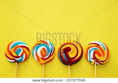 Colorful Hard Candy Lollipop On Yellow Pastel Background. Rainbow Sweet Pattern On Stick Flying Arou