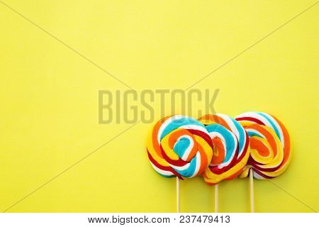Colorful Hard Candy Lollipop On Yellow Pastel Background. Rainbow Sweet Pattern On Stick Flying Arou
