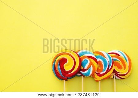 Colorful Hard Candy Lollipop On Yellow Pastel Background. Rainbow Sweet Pattern On Stick Flying Arou