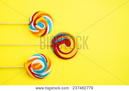 Colorful Hard Candy Lollipop On Yellow Pastel Background. Rainbow Sweet Pattern On Stick Flying Arou