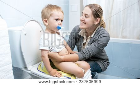 Portrait Of Smiling Mother Seatting Her Toddler Son On Toilet