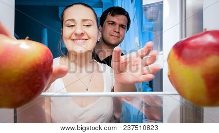 Portrait Of Happy Family Taking Apples From Refrigerator At Night