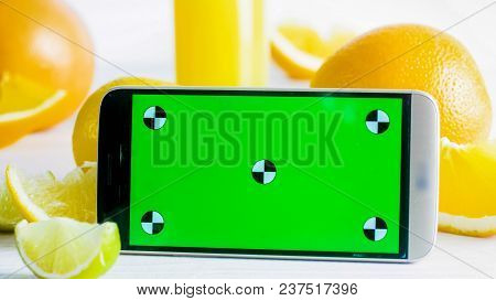 Closeup Image Of Mobile Phone With Green Chromakey Screen Next To Fresh Fruits On White Table. Perfe
