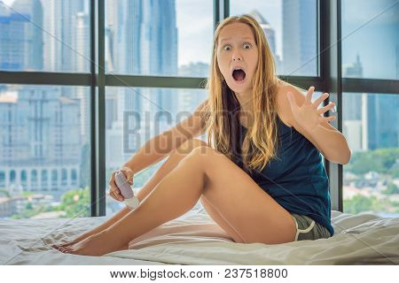 Young Woman Sitin On Bed At Home And Doing Epilation With Epilator On Legsand Is In Pain. On The Bac