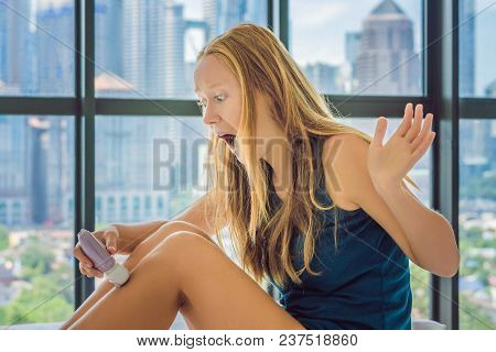 Young Woman Sitin On Bed At Home And Doing Epilation With Epilator On Legsand Is In Pain. On The Bac