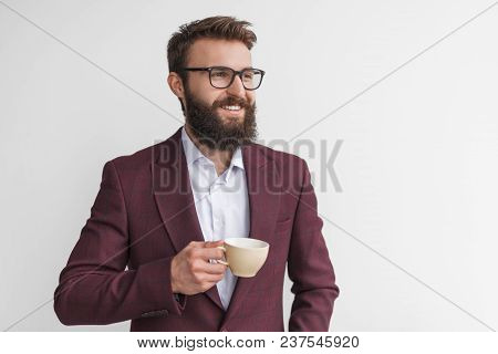 Stylish Bearded Businessman In Glasses And Trendy Suit Holding Coffee Cup Smiling Away On White.