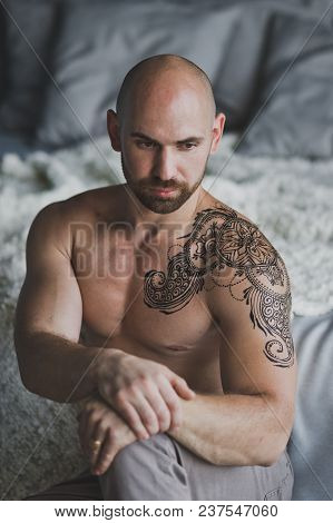 Bald Beefy Man With Naked Torso Sitting In The Room.