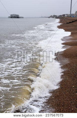 Brighton, United Kingdom - March 28 2018:   Waves Rolling In To The Stones Of Brighton Beach, With T