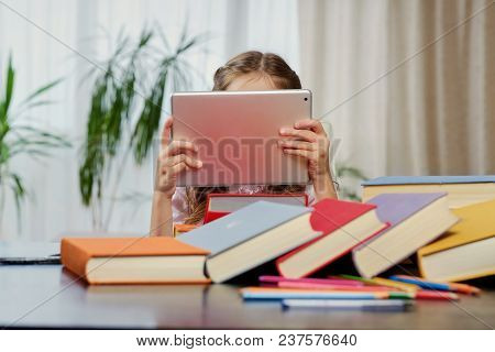 Little Girl Looking At The Tablet Pc In A Classroom. Colorful Books At The Table.