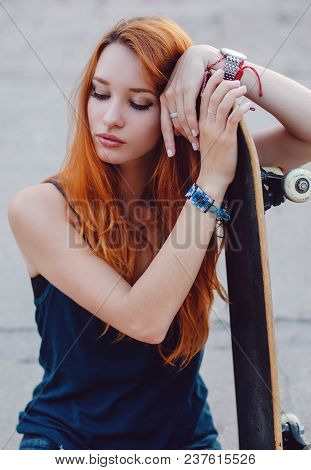 Redhead Slim Girl In Jeans Shorts And Black T Shirt Posing With Skateboard In Urban Sciene.
