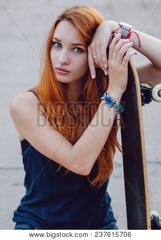 Redhead Slim Girl In Jeans Shorts And Black T Shirt Posing With Skateboard In Urban Sciene.