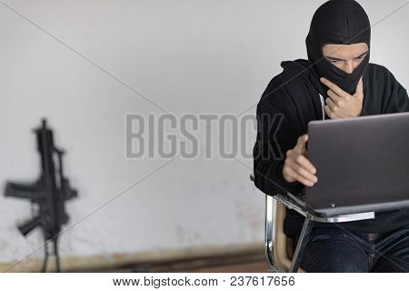 Black Masked Hacker In The Black Long Sleeve Shirt Is Sitting On The Desk In Front Of Laptop And Thi