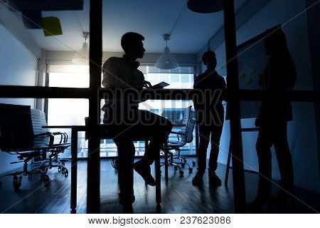 Silhouette Of Young Business People Discussing About Their Business Plan At Modern Startup Office. M