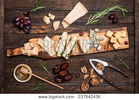 Cheese Platter With Different Cheeses, Grapes, Nuts, Honey, Bread And Dates On Rustic Wooden Backgro