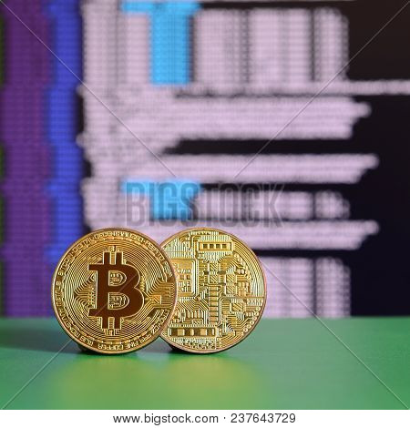 Two Gold Bitcoins Lie On The Green Surface On The Background Of The Display, Which Shows The Process