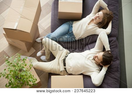 Relaxed Smiling Couple Resting On Couch Moved In New Home With Boxes, Happy Real Estate Renters Owne