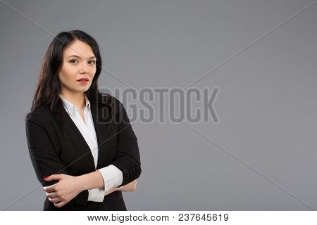 Standing Businesswoman Portrait On Light Grey Background And Looking At Camera. Copy Space On Right