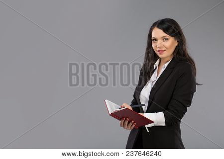 Young Business Woman Writing Down Notes To Notepad. Pretty Thoughtful Business Lady Writing On Clipb