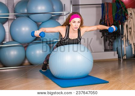 Woman Exercising With Dumbbells On A Fitness Ball.