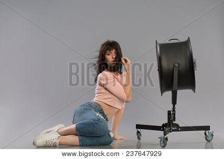 Young Sexy Female Model Posing With Working Wind Machine On Grey Background