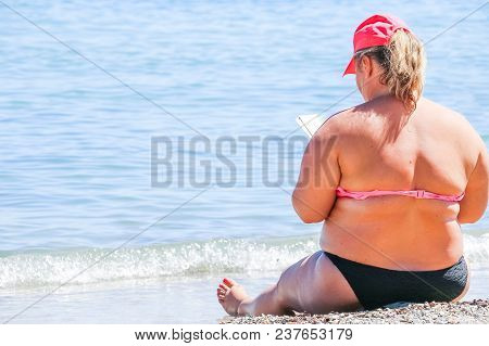 A Woman Wearing A Hat, Sitting On The Beach Staring At The Sea