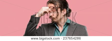 Handsome young man with sleepy expression, being overworked and tired, rubbes nose because of weariness