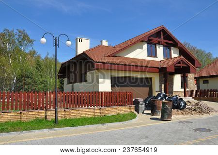 Modern House With Attic, Garage And Fencing With Lots Of Building Construction Garbage In Gabage Bag