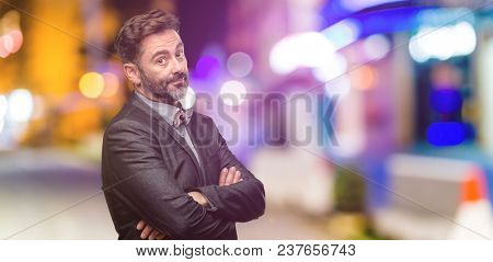 Middle age man, with beard and bow tie with crossed arms confident and happy with a big natural smile laughing at night club