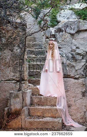 Young White Pixie Queen In A Crown With A Veil And A Long Dress Down The Stone Stairs In A Fabulous 