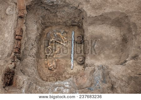 Archaeological Excavations. Top View Of The Burial Of A Person, Bones, Skull With Two Ritual Ceramic