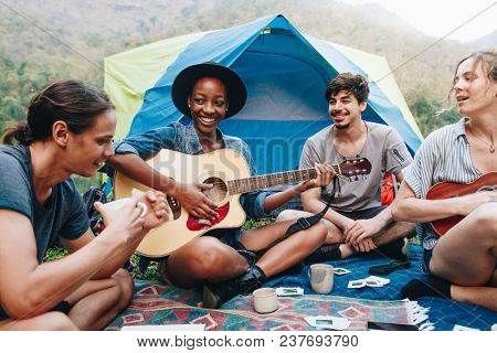 Group of young adult friends in camp site playing guitar and ukelele and singing together outdoors recreational leisure and friendship concept