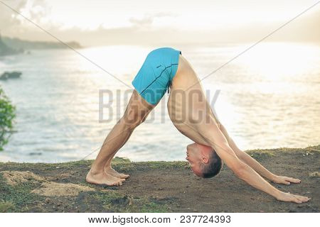 Handsome Man Doing Yoga Near The Beach With Blue Sky And Sea Background. Relaxing And Healthy Lifest