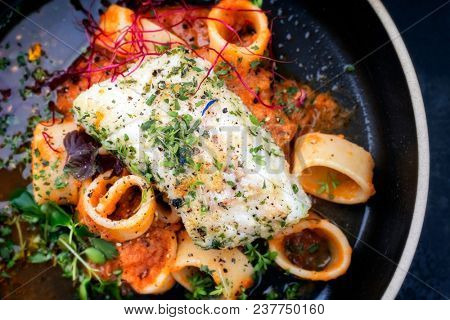 braised codfish filet and lettuce and herbs with calamarata noodles as top view on a plate